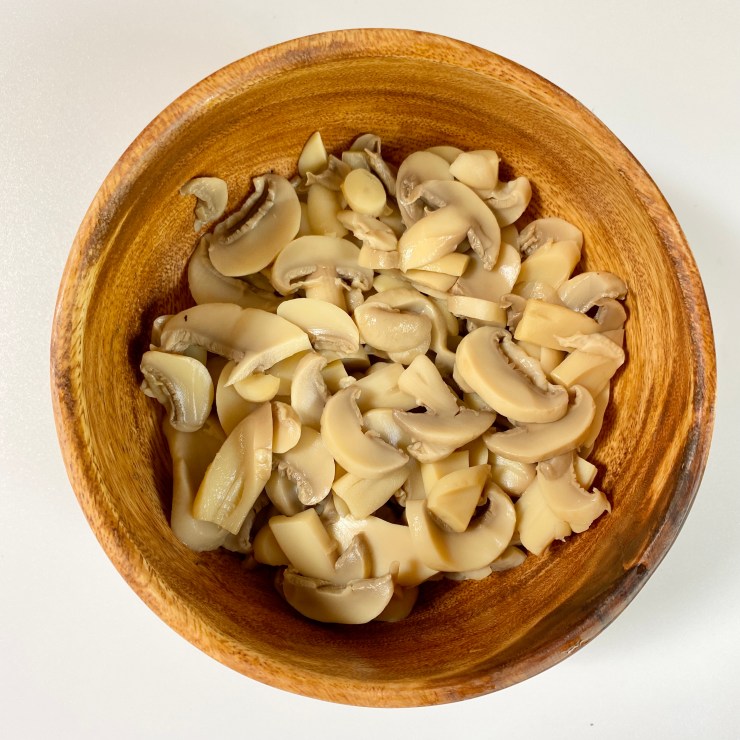 Sliced button mushrooms in a wooden bowl