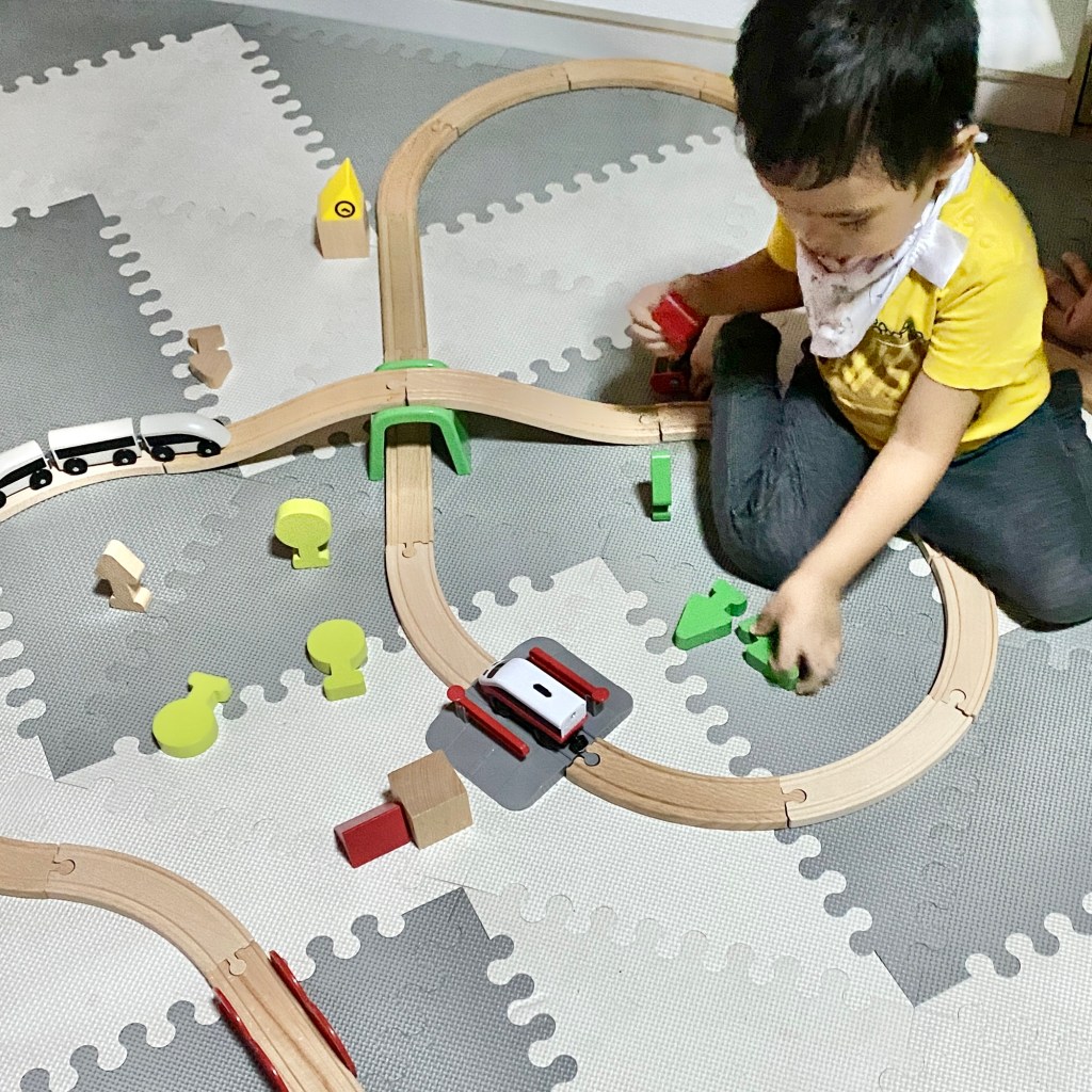 Toddler playing with wooden train tracks and toys