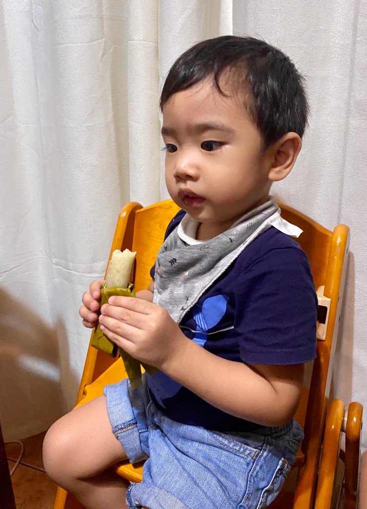 Little boy eating suman on a Japanese wooden high chair.