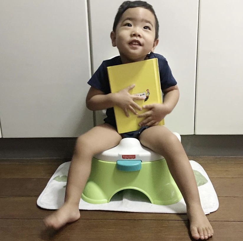 Little boy hugging a book while on a potty