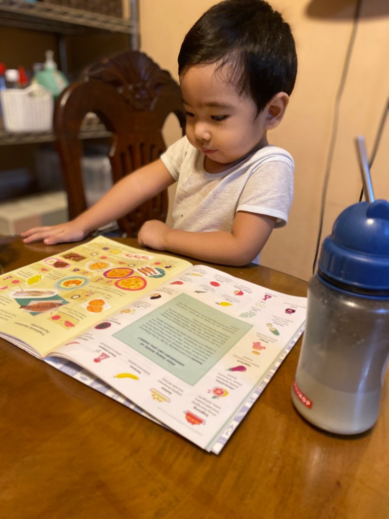 Little boy reading a book with a bottle of milk.