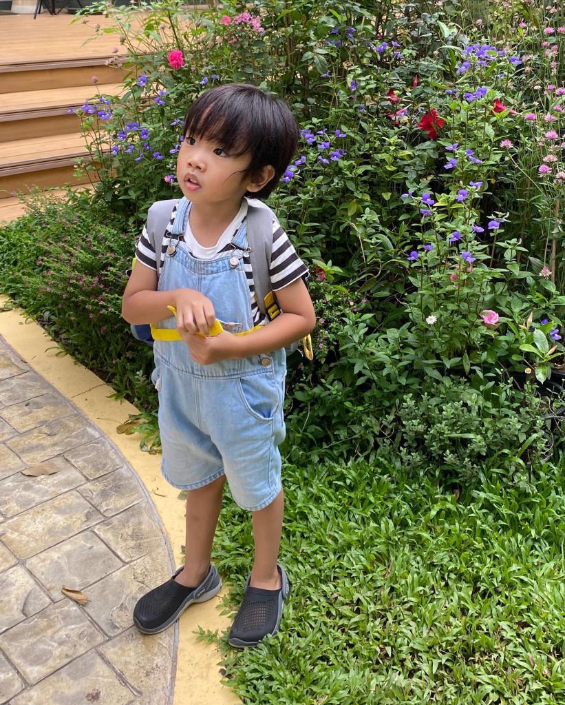 Little boy standing by flowers wearing short dungarees