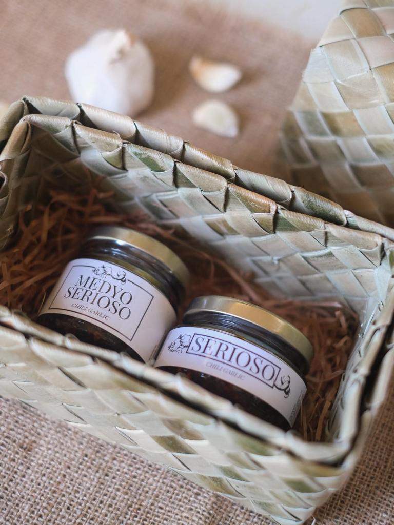 Two chili garlic sauce bottles on a native woven box with brown shredded paper