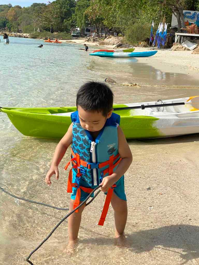 little boy wearing a life vest playing on the beach