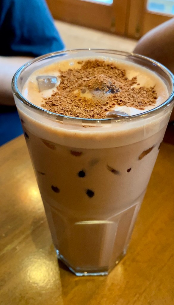 a glass of cold chocolate drink with milk foam and cacao powder on top