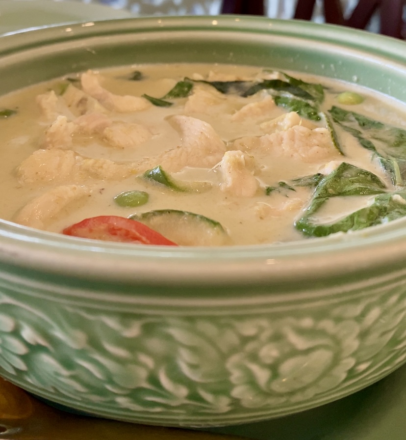 A bowl of green curry with chicken and basil leaves