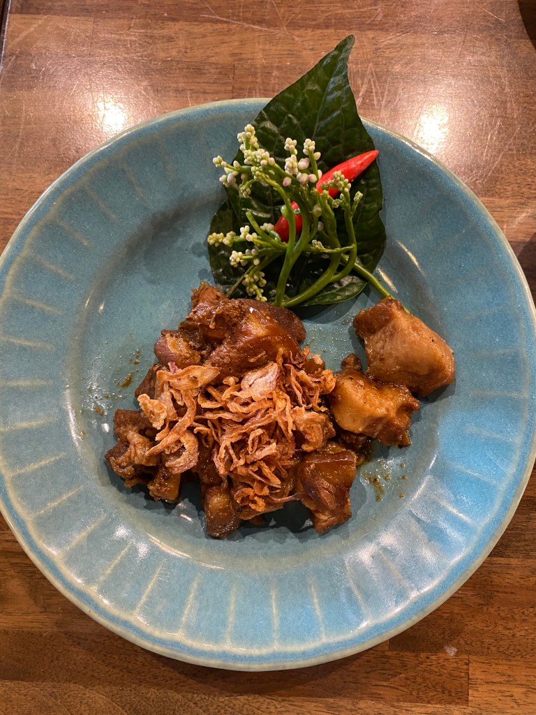 A blue plate with pork belly in sweet sauce topped with fried shallots with a leaf and chili garnish