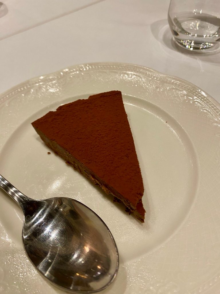 A white plate with a slice of chocolate tart and a spoon