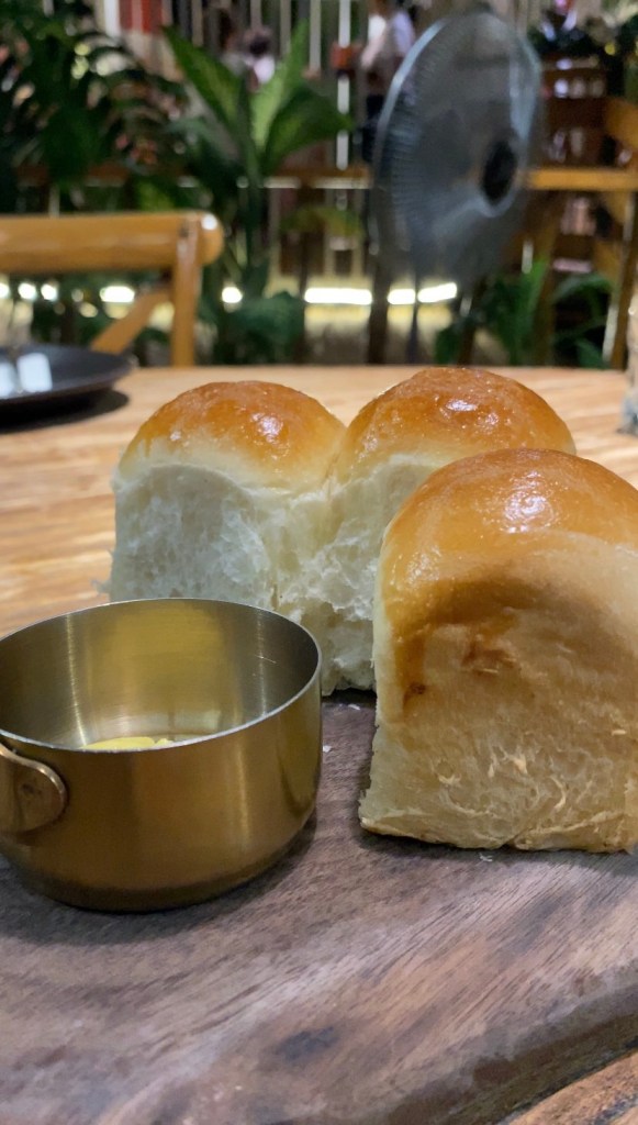 A wooden plate of dinner rolls with a tiny pot of herbed butter