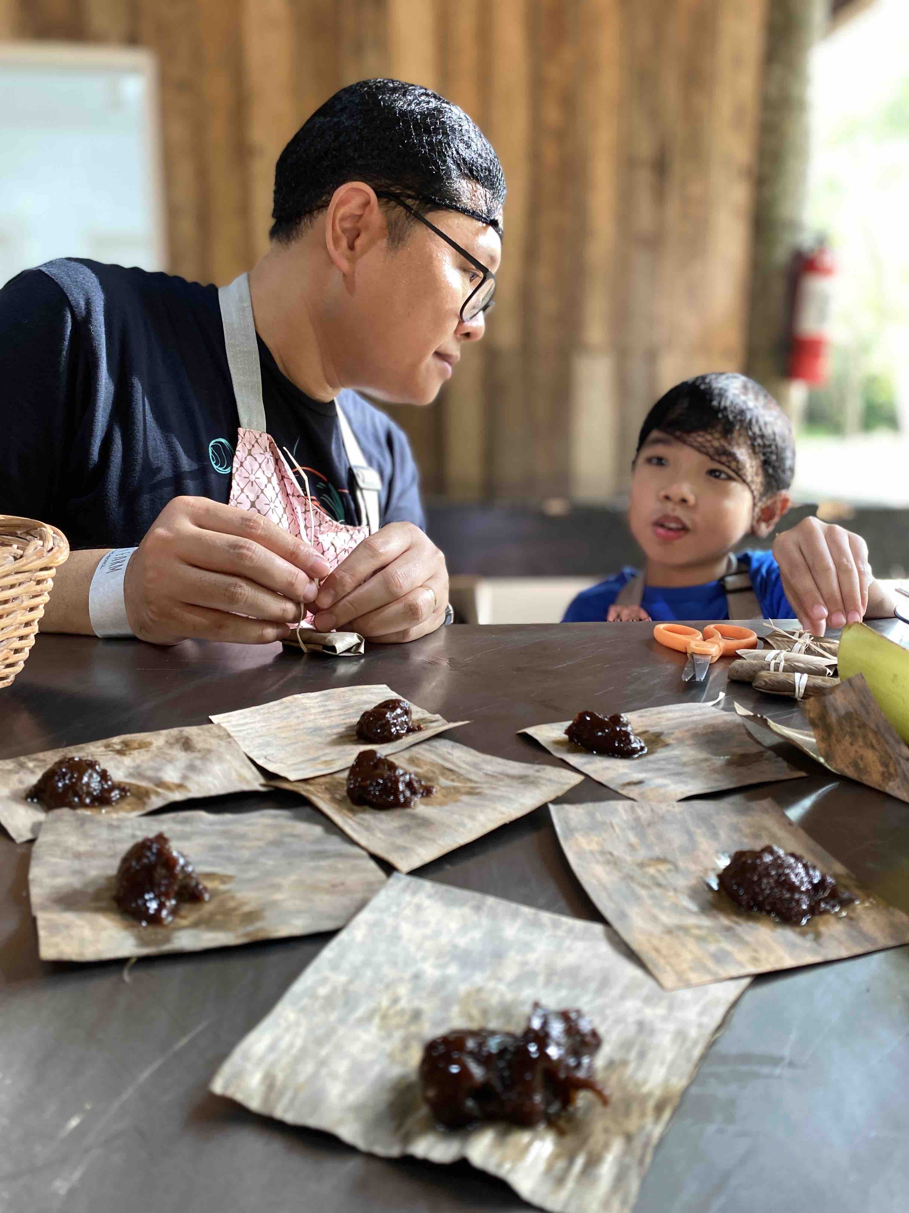 Father and son talking while wrapping coconut candy with dried banana leaves