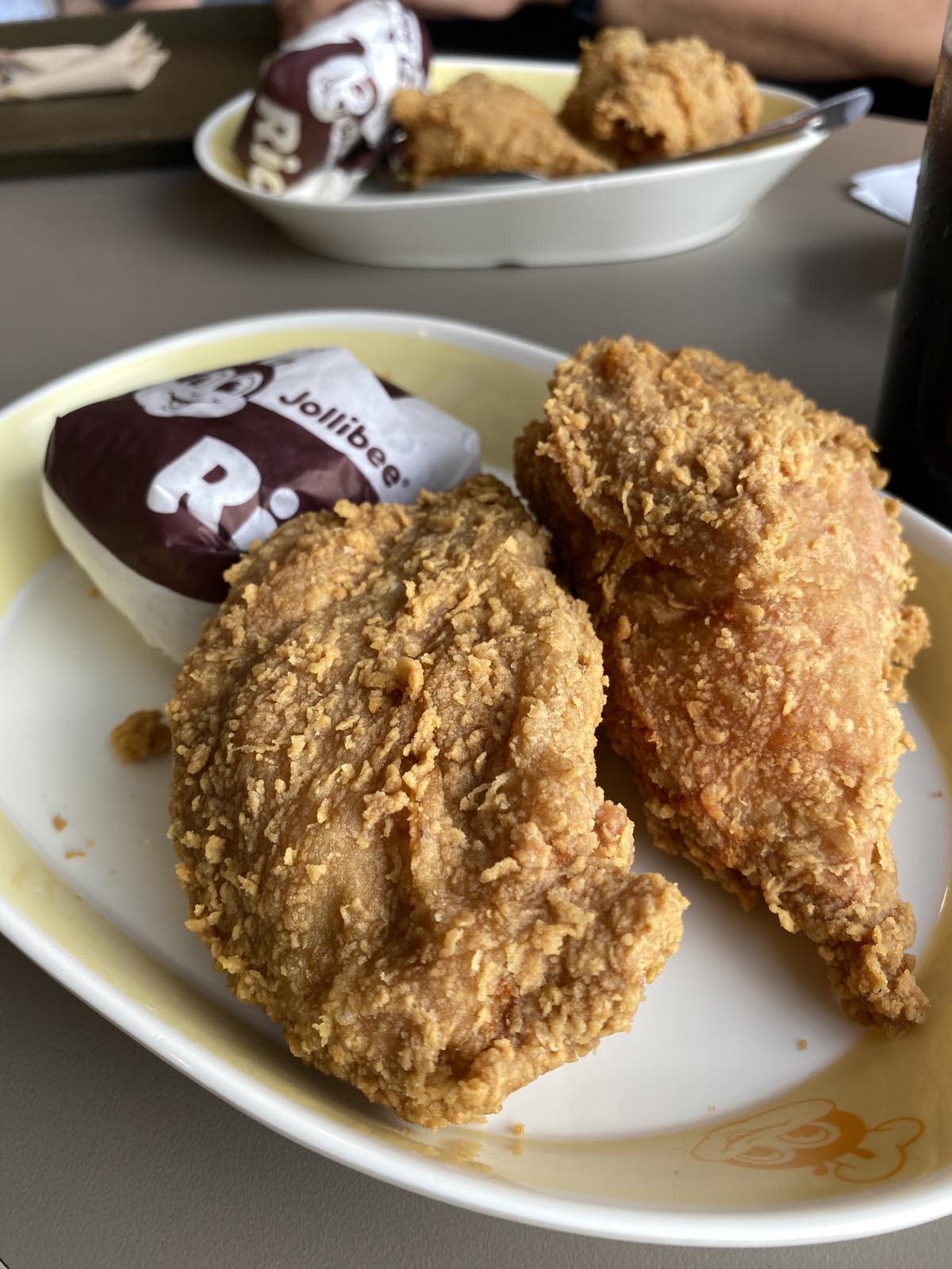 A plastic plate with two pieces of fried chicken and a wrapped cup of rice