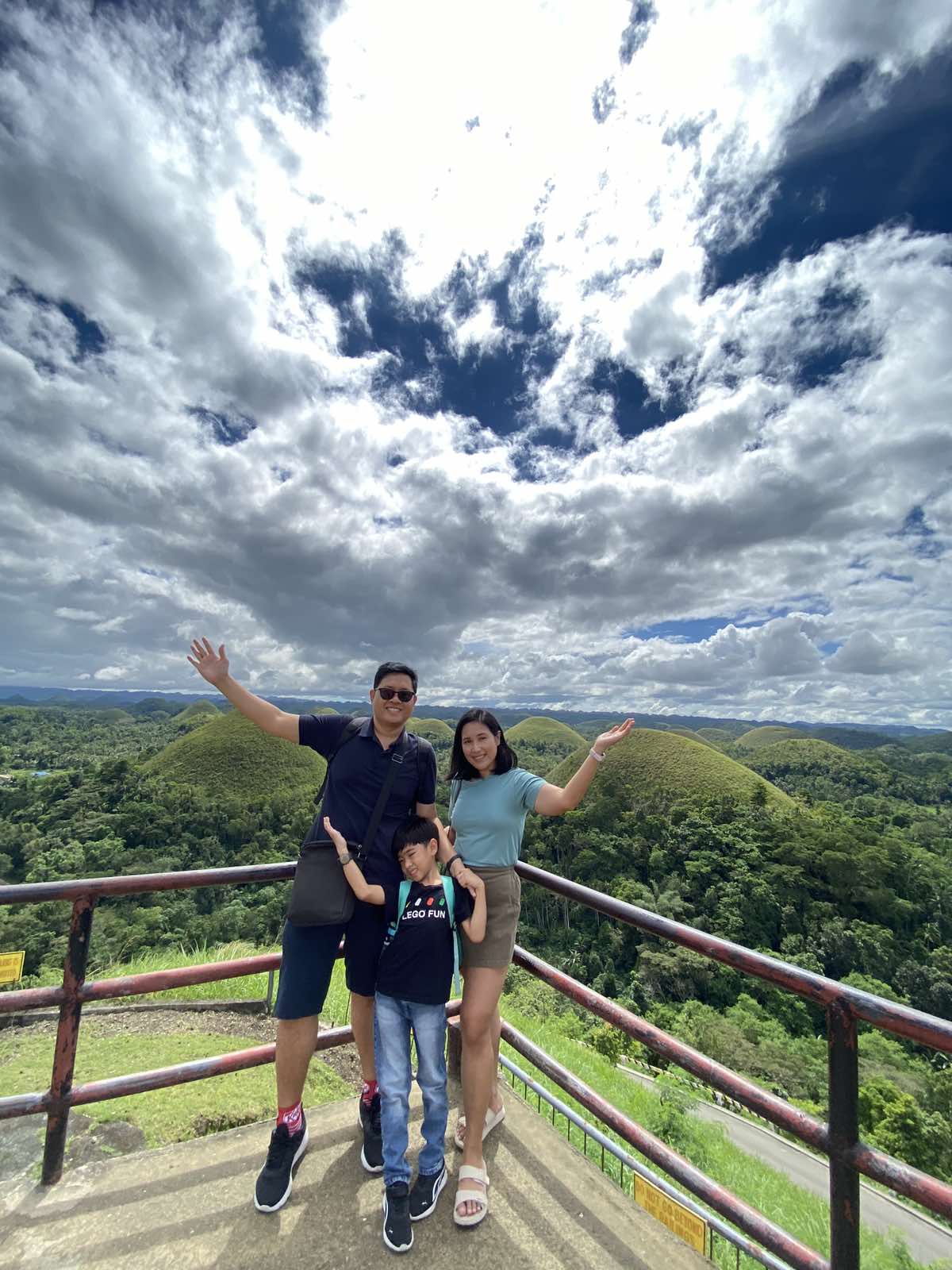Family of three posing for a photo with the Bohol Chocolate Hills behind them