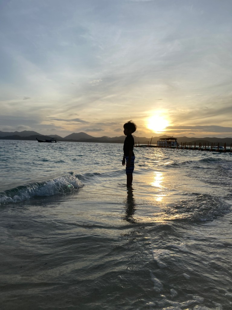 A silhouette of a boy standing on a beach during sunrise