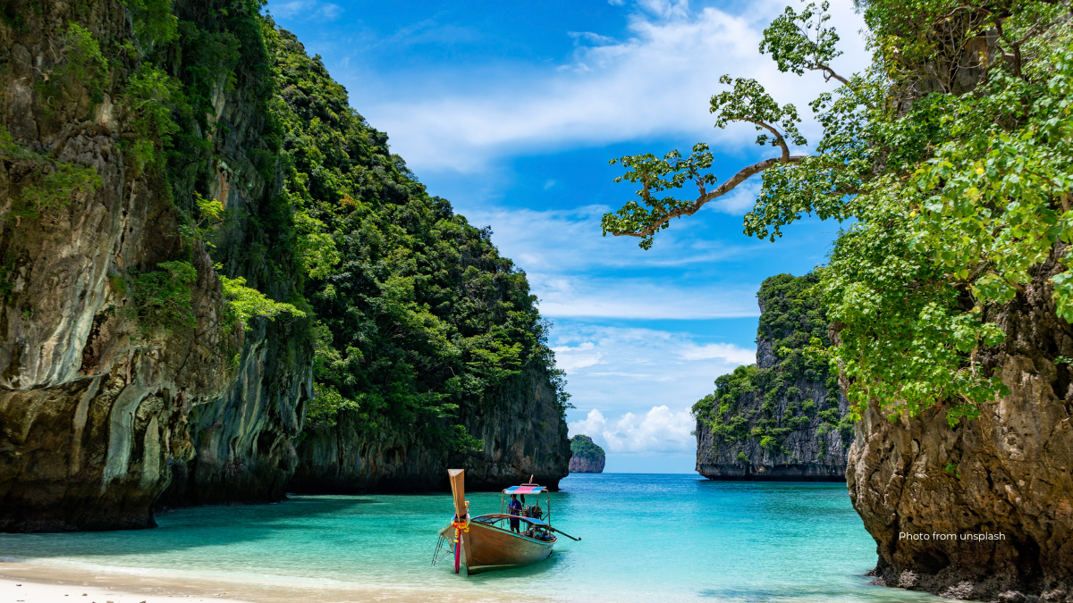 A picture of a Thai long tail boat on a beach with clear blue water in the middle of cliffs