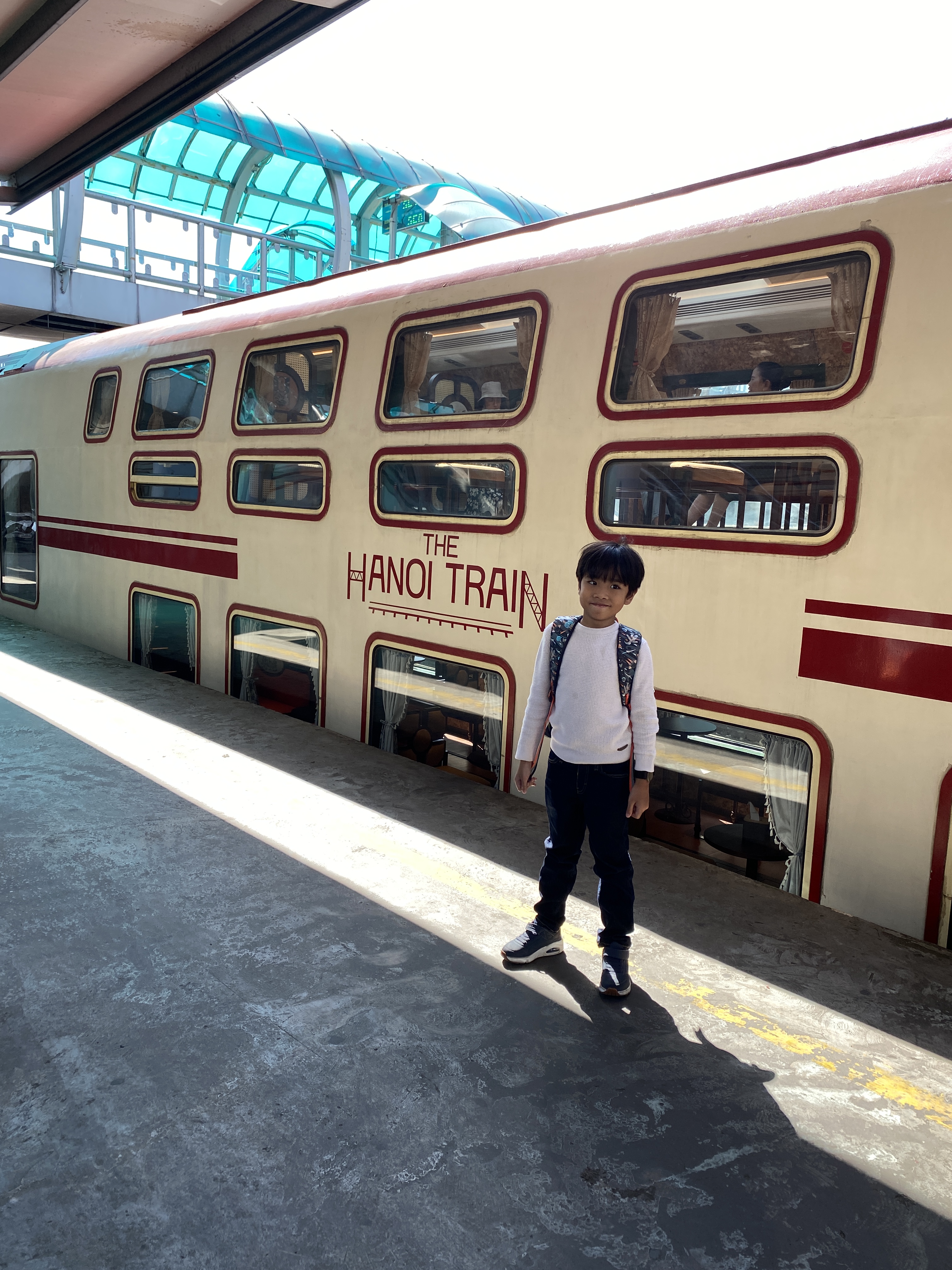 A boy standing in front of a cream and red colored vintage looking Hanoi Train