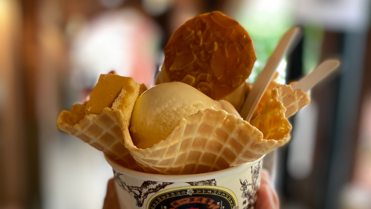 A cup of ice cream on a crisp waffle cone topped with a circle almond brittle