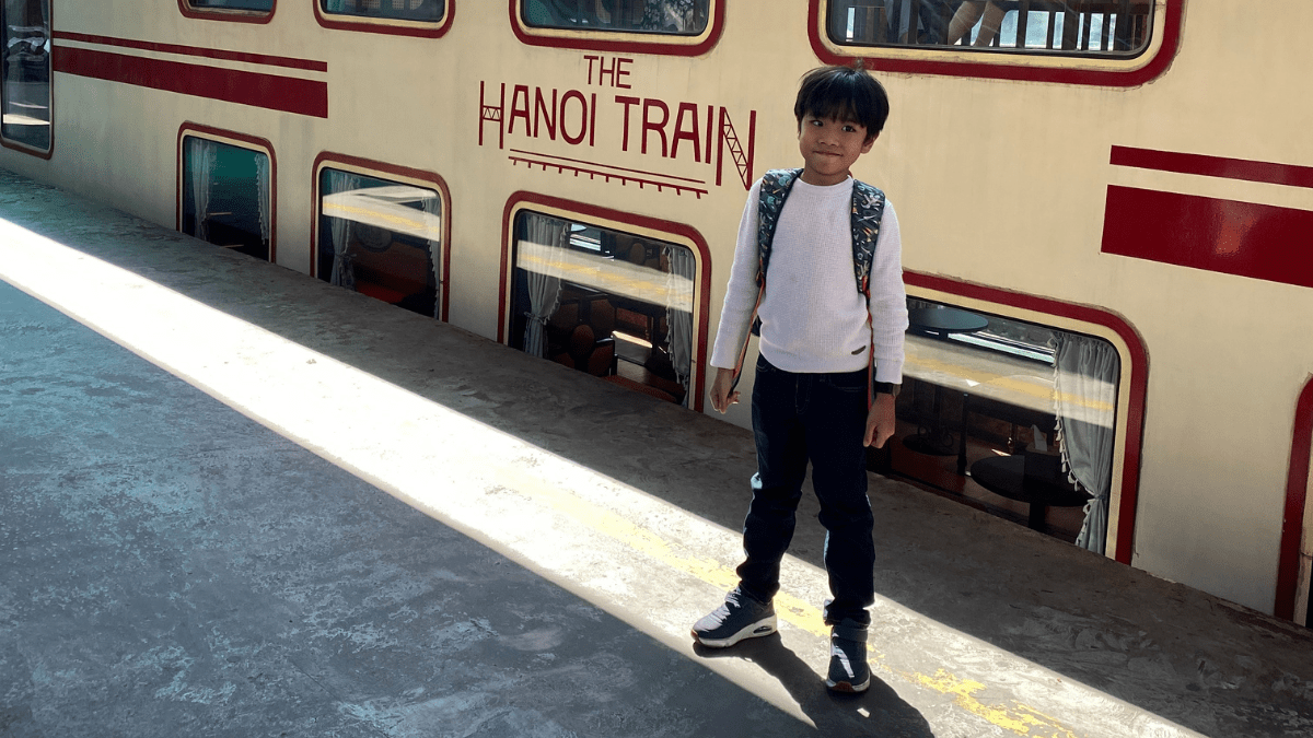 A boy standing in front of a cream and red vintage looking Hanoi Train